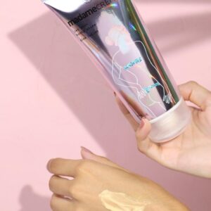 mãos segurando o hidratante iluminador glow lotion da madamecrème mostrando a embalagem e textura do produto