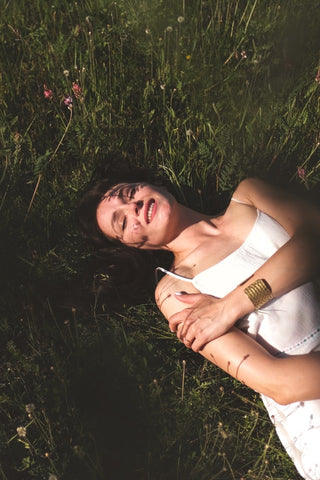 mulher sorrindo deitada sobre a relva com a luz do sol no corpo