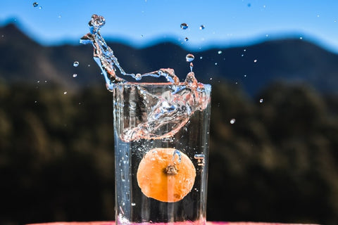 copo de vidro cheio de água com uma tangerina submersa