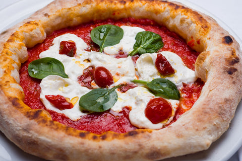 pizza com molho de tomate, queijo, tomates e folhas de manjericão