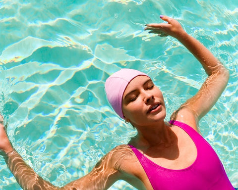 mulher com maiô rosa boiando na piscina com olhos fechados